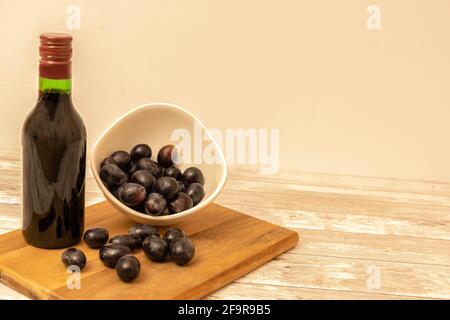 Fuoco selettivo di una bottiglia di vino rosso con uve rosse in una ciotola e su un asse di legno da cui la bevanda alcolica è presa per accompagnare i pasti. Foto Stock