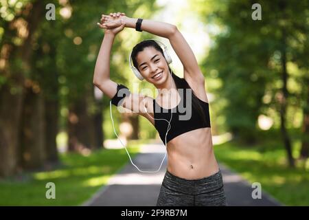 Donna asiatica atletica in abbigliamento sportivo facendo esercizi di stretching all'aperto, allenamento nel parco Foto Stock