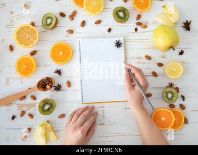 La mano femminile scrive in taccuino vuoto su sfondo sano di cibo, vista dall'alto, piatto, spazio di copia Foto Stock