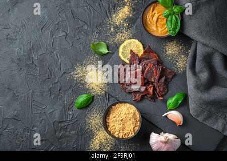 Manzo a scatti con senape, aglio e basilico su sfondo nero. Vista dall'alto, spazio di copia. Foto Stock