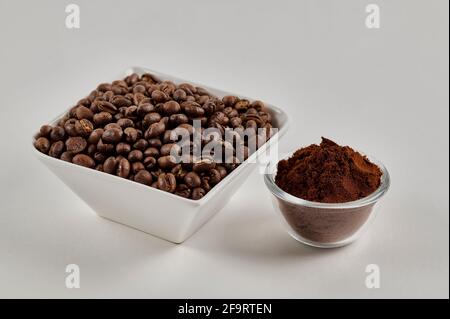 Chicchi di caffè interi alla pesciolina e polvere di caffè appena macinata su sfondo bianco Foto Stock