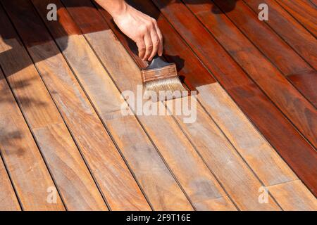 IPE legno duro deck annuale rinfrescante, la mano del lavoratore sta olando terrazza coperta con una spazzola di pittura dopo la levigatura Foto Stock