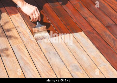 IPE legno duro deck annuale rinfrescante, la mano del lavoratore sta olando terrazza coperta con una spazzola di pittura dopo la levigatura Foto Stock