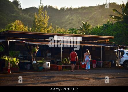 Shopping per giovani coppie durante il tramonto presso lo stand del mercato agricolo a bordo strada presso le fattorie di Kahuku Land, North Shore di Oahu, vicino al Turtle Bay Resort, Hawaii, USA Foto Stock