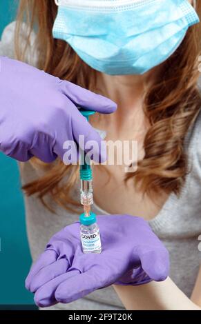 Infermiere medico di sesso femminile che tiene il flaconcino di vaccino di covid-19 sulla siringa che indossa guanti in lattice e maschera facciale Foto Stock