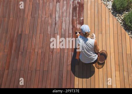 Sopra la vista del bel giardino di ristrutturazione, operaio mestieri donna sta olando un ponte, terrazzo legno ponte processo di restauro macchie Foto Stock