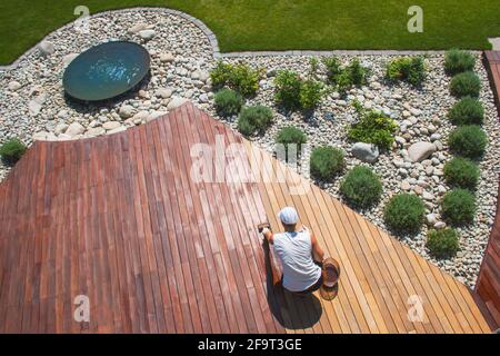 IPE legno duro ponte annuale rinfrescante, una persona sta olando terrazza coperta con un pennello dopo la levigatura Foto Stock