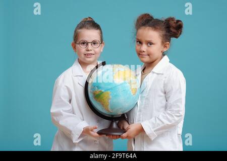 Ritratto di due bambine che tengono grande mondo globo e. sorridendo con la fotocamera sullo sfondo blu Foto Stock