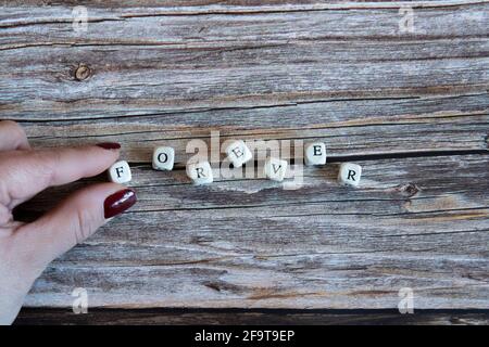 Le dita delle donne che mettono dadi che formano la parola 'per sempre' su uno sfondo di legno. Spazio di copia Foto Stock
