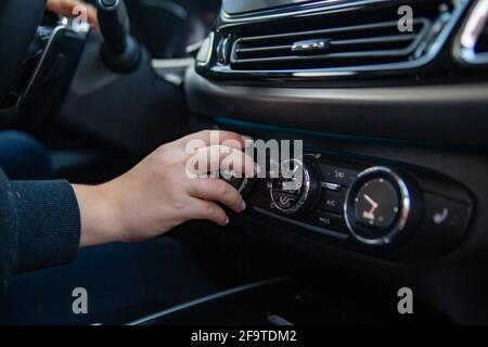 La mano della donna commuta l'aria condizionata nella vettura. Il conducente accende l'impianto di climatizzazione dell'auto. Sistema di climatizzazione moderno di qualità superiore Foto Stock