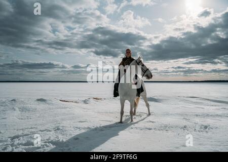 Giovane donna vichinga con capelli rossi cavalcano un cavallo. Luce straordinaria. Gioco di ruolo Foto Stock