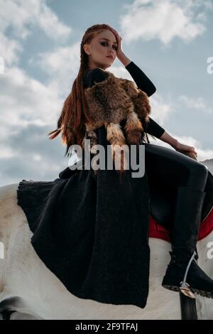 Giovane donna vichinga con capelli rossi cavalcano un cavallo. Luce straordinaria. Gioco di ruolo Foto Stock