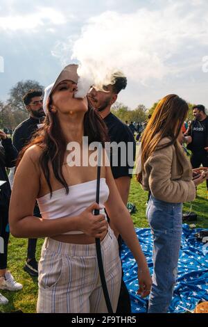 Londra, Regno Unito 4 aprile 2021 migliaia di persone si riuniscono ad Hyde Park per celebrare il 4/20 'Weed Day' nonostante le restrizioni del Covid. La giornata celebra l'uso della cannabis e chiede che sia legalizzata. Una donna esala fumo da un tubo di narghilè Foto Stock