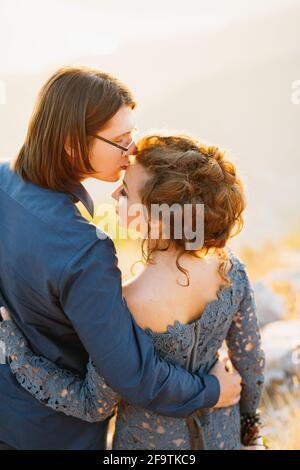 La sposa e lo sposo abbracciando il monte Lovcen, lo sposo bacia la sposa sulla fronte, vista posteriore Foto Stock