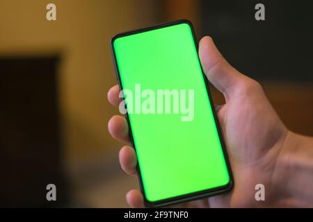 Mano umana isolata che tiene uno smartphone con schermo verde, dipendenza hi-tech concetto Foto Stock