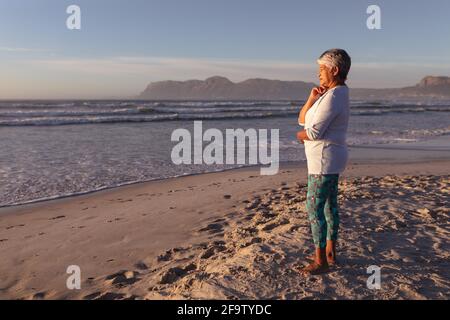 Donna afro-americana pensierosa con la mano sul mento in piedi sulla spiaggia Foto Stock