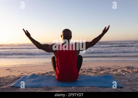 Vista posteriore dell'uomo afro-americano anziano con le braccia larghe aperto praticando yoga in spiaggia Foto Stock