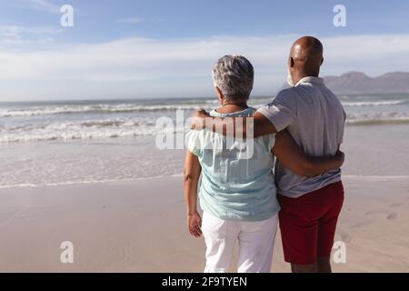 Vista posteriore della coppia afro-americana più anziana che si agganava l'un l'altro sulla spiaggia Foto Stock