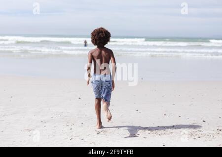 Vista posteriore del ragazzo afroamericano che corre sulla spiaggia Foto Stock