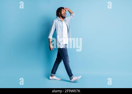 Vista laterale del profilo della dimensione del corpo di lunghezza intera di bella allegra guy walking guardando lontano isolato su sfondo di colore blu brillante Foto Stock