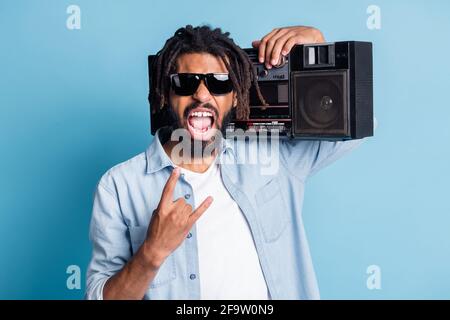Ritratto di attraente pazzo allegro ragazzo cool che trasporta giocatore mostrando corno divertente isolato su sfondo di colore blu brillante Foto Stock