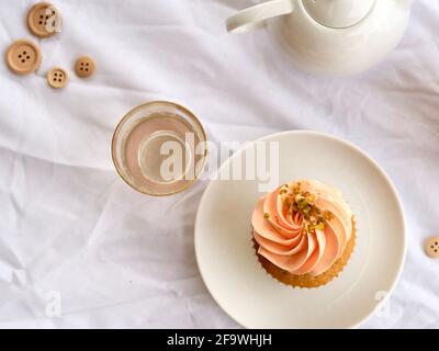 Bella cupcake rosa e vetro rosa con teiera su a. sfondo bianco luminoso Foto Stock