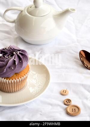 Cupcake con glassa viola e teiera bianca su un bianco sfondo testurizzato Foto Stock