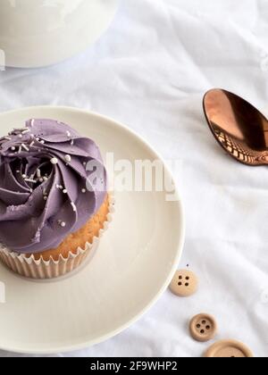 Cupcake con glassa viola su uno sfondo bianco brillante e testurizzato Foto Stock