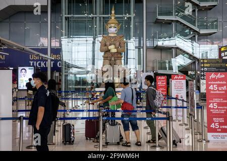 I passeggeri arrivano per il check-in del volo mentre una tradizionale statua tailandese indossa una maschera facciale all'aeroporto Suvarnabhumi di Bangkok, Thailandia, l'8 marzo 2021 durante la pandemia globale del covid-19. Foto Stock