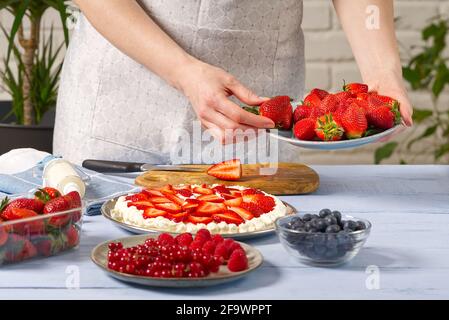 donna panettiere impila fragole sulla base meringa torta di fragole. Torta di fragole fatta in casa con torta di meringa e crema con fragole. Foto Stock