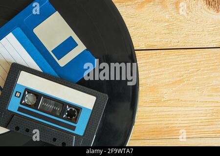 Sul disco in vinile sono presenti una cassetta audio e un floppy disk. Il disco stesso giace su uno sfondo di legno. Vista dall'alto. Spazio per il testo Foto Stock