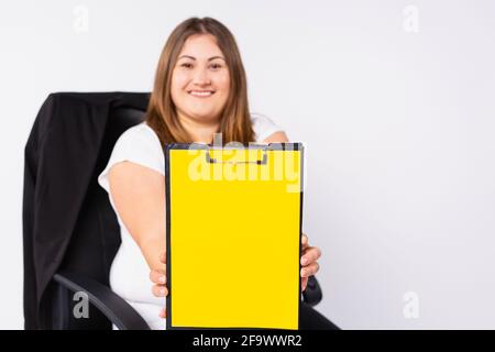 Bella giovane più dimensione, donna di affari tiene una clipboard con mock up illuminando spazio vuoto isolato su sfondo grigio. Raggiungere la ricchezza di carriera Foto Stock