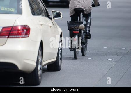Magonza, Germania. 13 Apr 2021. Un'auto si avvicina dietro un ciclista. La tendenza verso le biciclette e le e-bike, che è cresciuta in modo significativo durante la pandemia di Corona, sta sfidando le cinque città più grandi della Renania-Palatinato. Secondo un'indagine dpa, la quota del traffico in bicicletta dovrebbe essere aumentata ovunque. (A dpa 'divieto di sorpasso e parcheggio auto a più piani: Le città si preparano per il boom della bicicletta') Credit: Sebastian Gollnow/dpa/Alamy Live News Foto Stock
