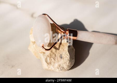 Rullo facciale in quarzo rosa cristallo su pietre, sfondo in marmo. Massaggio viso anti-age per un trattamento naturale di sollevamento e tonificazione a casa. Conce di bellezza Foto Stock