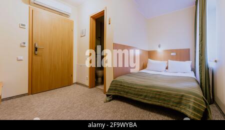 Interno di una camera d'hotel semplice e ben arredata camera con letto matrimoniale durante il giorno Foto Stock