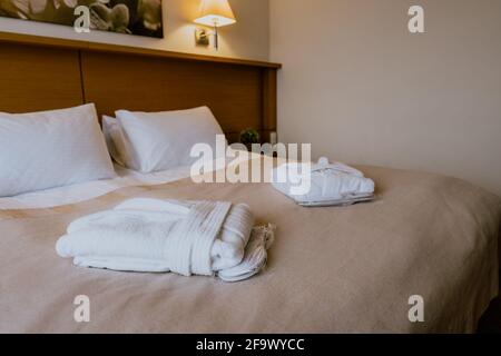 Interno di una camera d'hotel semplice e ben arredata con accappatoi ripiegati su un letto matrimoniale Foto Stock