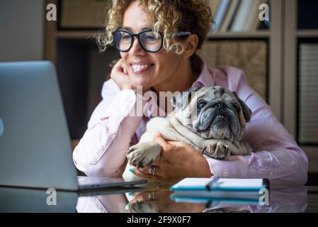 Donna adulta lavora al computer portatile a casa in ufficio con il suo cane migliore bella amico pug - concetto di donne moderne e lavoro intelligente nuovo lavoro Foto Stock