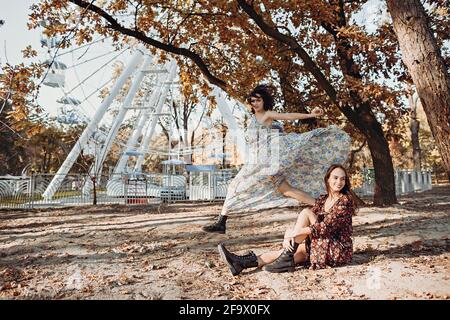 Due giovani donne in abiti vintage che si divertono nel parco vicino alla ruota di rinvio Foto Stock