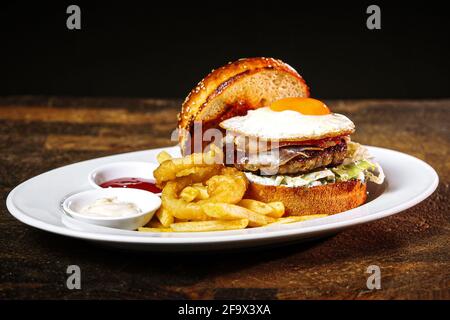 Primo piano di un hamburger fresco e fritto con anelli di cipolla e salse diverse Foto Stock