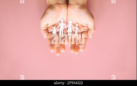 Mano che tiene la carta di famiglia tagliata su sfondo rosa. Concetto di giornata della famiglia, cura di promozione, violenza domestica, homeschool, giornata internazionale delle famiglie, mondo Foto Stock