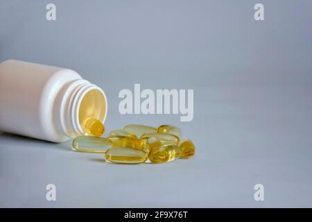 Capsule di gelatina traslucide omega 3 di colore giallo naturale in un vaso di plastica aperto capovolto sulla parte anteriore del tavolo. Concetto di medicina alternativa di farmaci, compresse Foto Stock