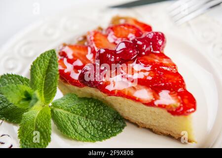 fetta di torta di fragole con fragole fresche e foglie di menta su piatto d'epoca, primo piano foto Foto Stock