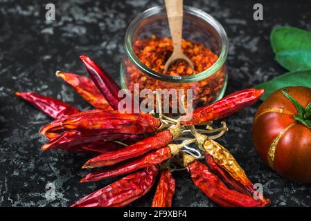 Peperoncini rossi in mazzo, peperoncini piccanti in ciotola di vetro, pomodoro e foglia su fondo nero, primo piano. Foto Stock
