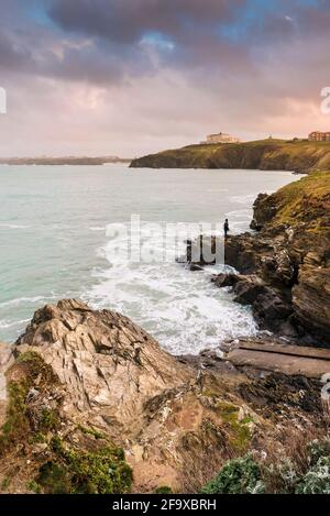 Calda luce serale su un pescatore che pesca al largo delle rocce sulla costa di Newquay Bay in Cornovaglia. Foto Stock