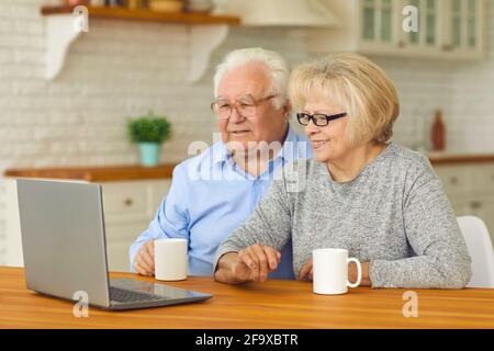 Felice coppia matura seduta di fronte al computer portatile a. nipoti di casa e videochiamata Foto Stock