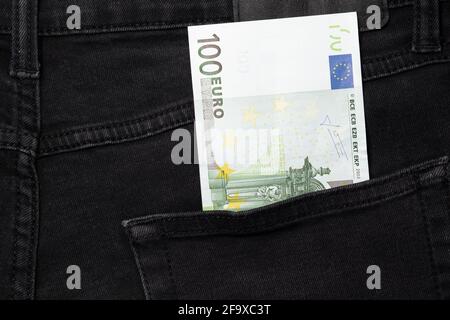 Un conto di cento euro che si stacca dalla tasca dei jeans neri Foto Stock