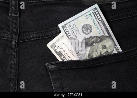 Centocinque banconote da dollaro che escono dalla tasca dei jeans neri Foto Stock