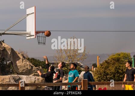 In un segno di declino COVID restrizioni un gruppo di giovani uomini giocare a pallacanestro in un parco di quartiere nella zona di San Francisco Bay. Foto Stock