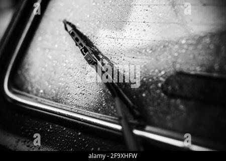 Immagine in bianco e nero di un lunotto di un'auto bagnata dalla pioggia con un tergicristallo scuro. Tempo nuvoloso e sognante. Trasporto. Foto Stock