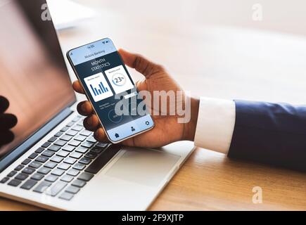 Uomo d'affari afro americano mano che tiene cellulare con app di trading Foto Stock